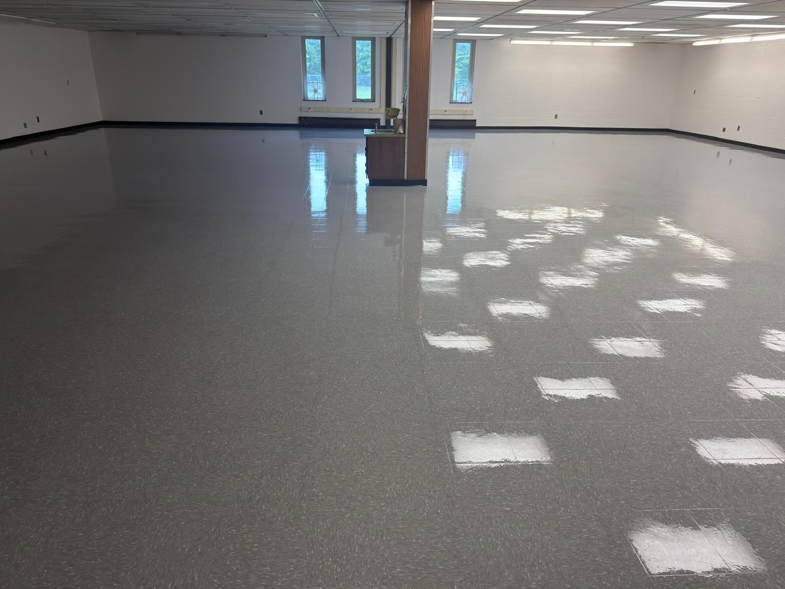 Large room with freshly waxed, high-gloss vinyl tile floor reflecting the ceiling lights