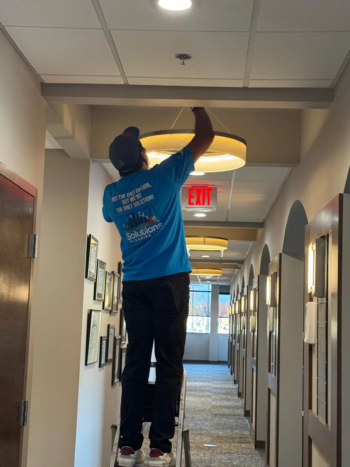 Solutions Cleaning team member on a ladder cleaning a hallway light fixture