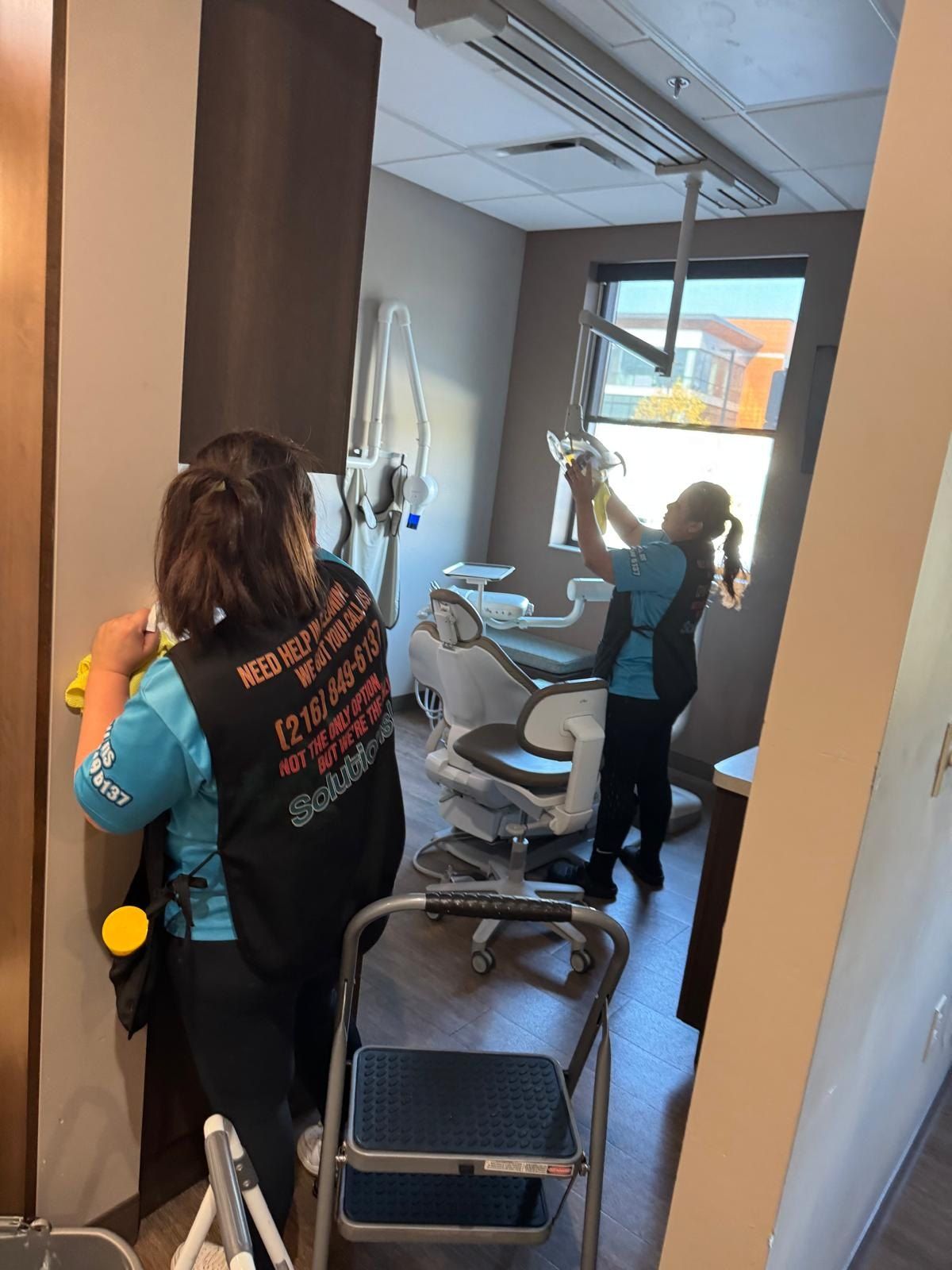 Two Solutions Cleaning team members cleaning a dental operatory, one dusting the overhead dental light